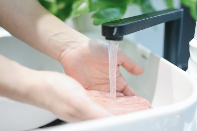 Person washing hands in a white sink with a black faucet